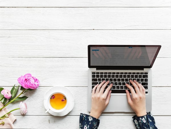 Hands typing on a latptop from above with flowers and tea